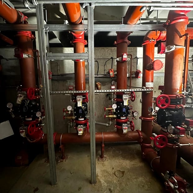 A bank of four sprinkler alarm valve sets on orange risers in a plant room, with gauges and tamper switched valves