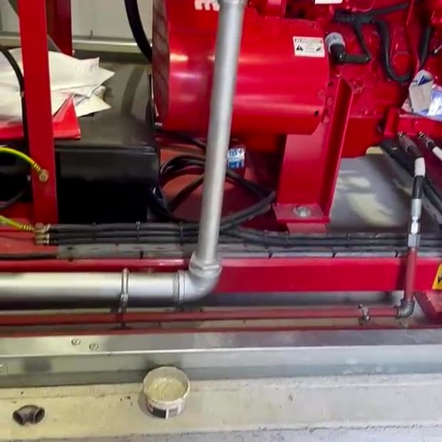 A red Clarke diesel fire pump set with its control panel and galvanised pipework in a pump room