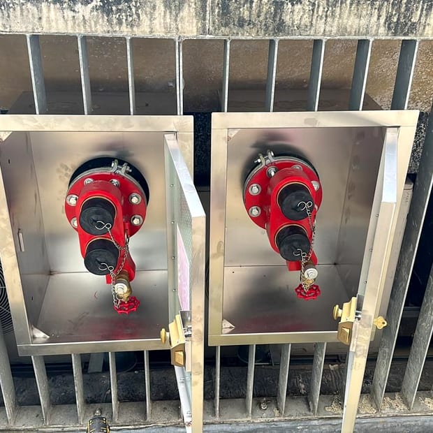 Two dry riser breeching inlets in stainless steel cabinets, twin instantaneous couplings with blank caps and chains