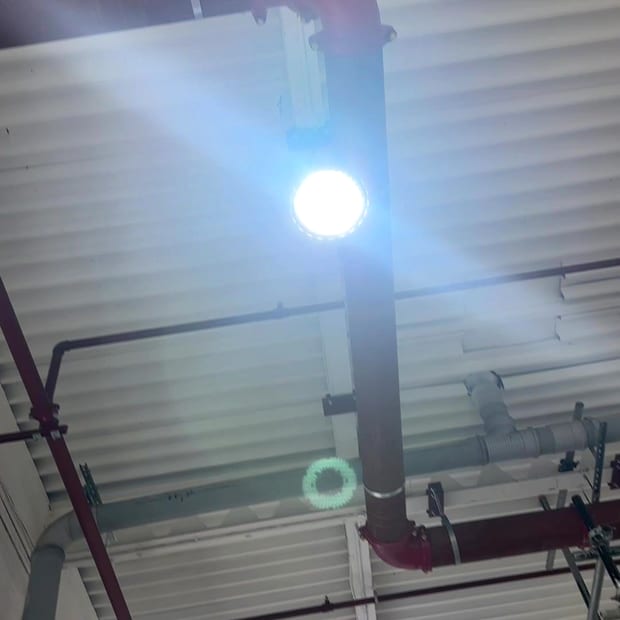 Sprinkler main under a metal deck, lit by a work light