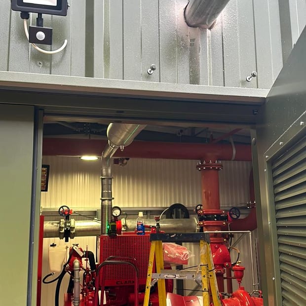 A packaged fire pump house with the door open, showing a red Clarke diesel pump set and its exhaust stack