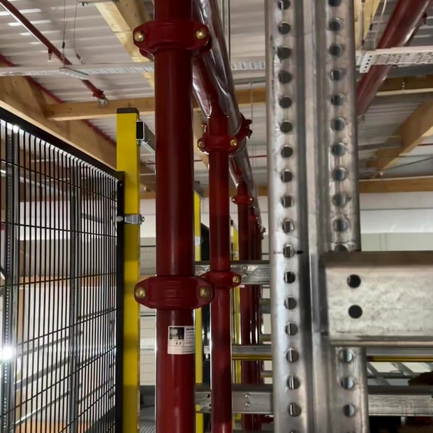 Riser pipework beside racking in a warehouse