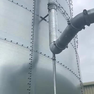 A large bolted sectional galvanised sprinkler tank with its overflow pipe and riser