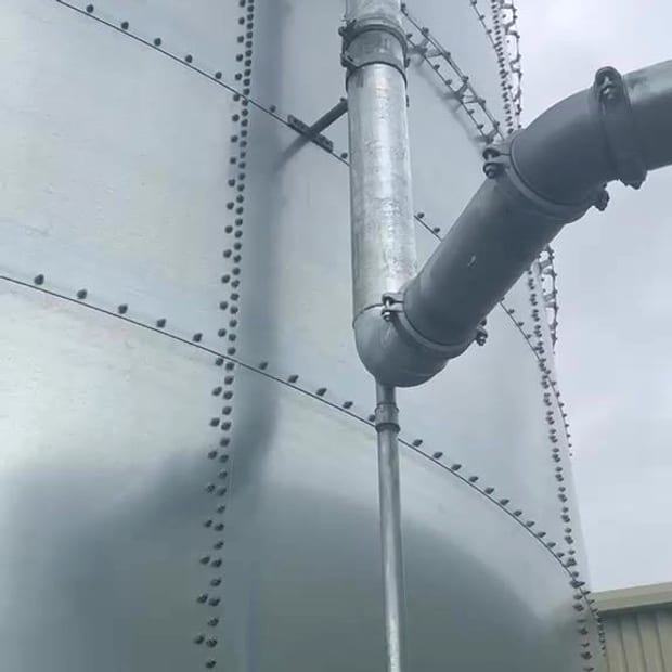 A large bolted sectional galvanised sprinkler tank with its overflow pipe and riser