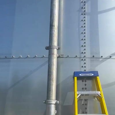 The bolted wall of a new sectional sprinkler tank with its galvanised riser, in sunlight