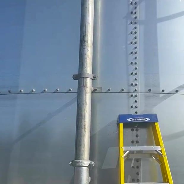 The bolted wall of a new sectional sprinkler tank with its galvanised riser, in sunlight